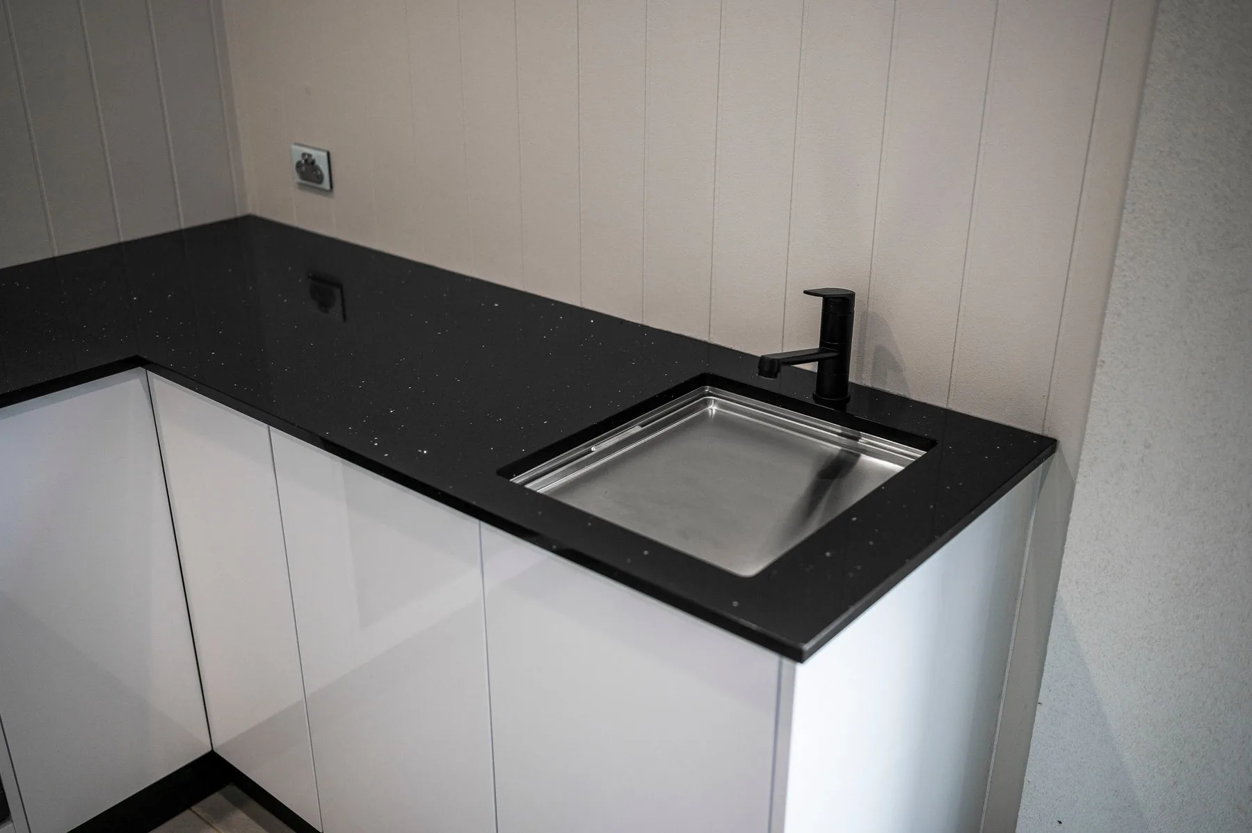 Stone benchtop with inset sink and black tapware in an alfresco kitchen
