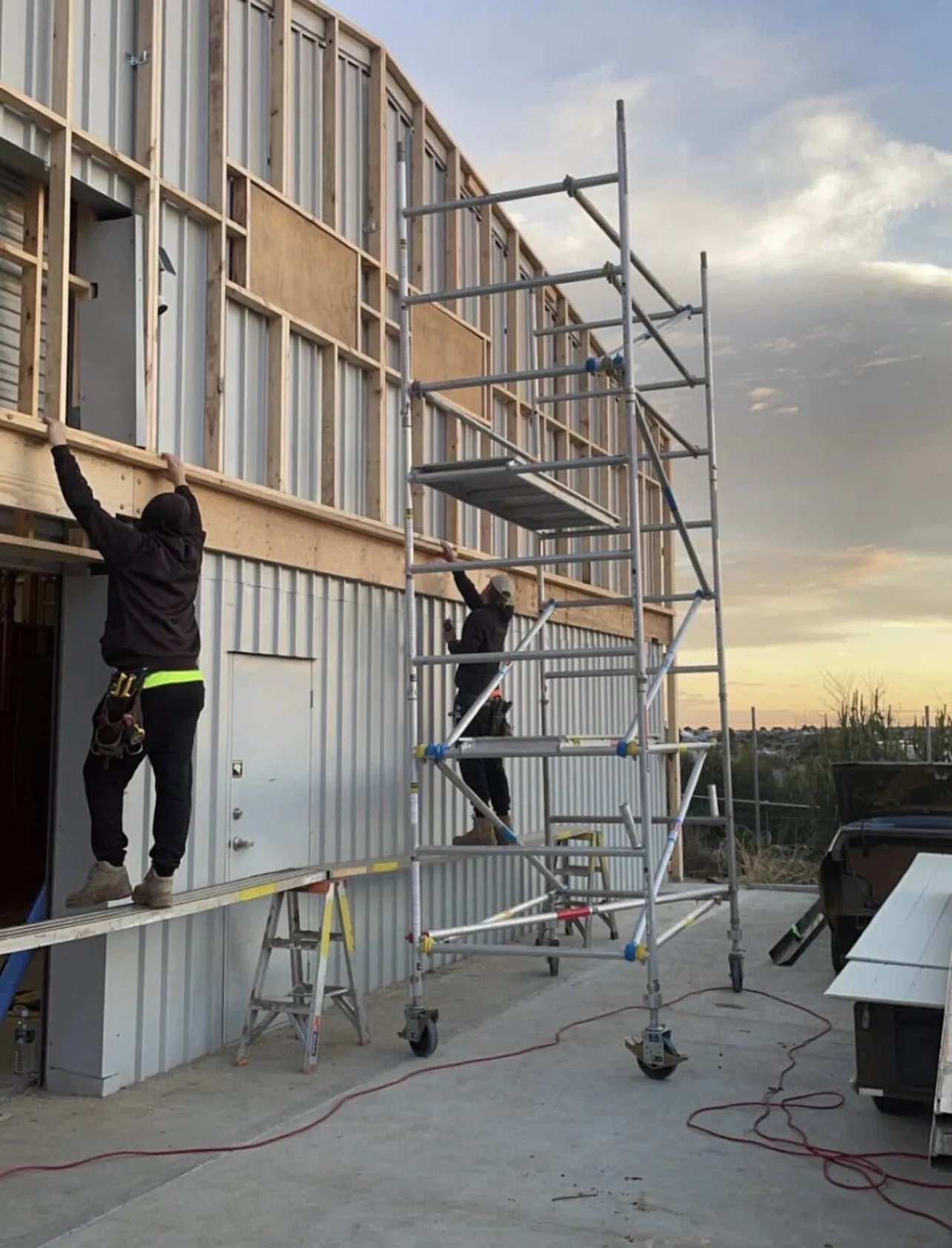 Carpenters cladding a two storey frame from scaffold at dusk
